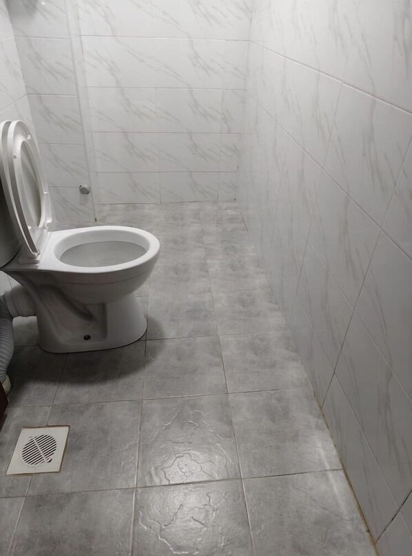 Un baño con inodoro, paredes de azulejos y un respiradero en el suelo.