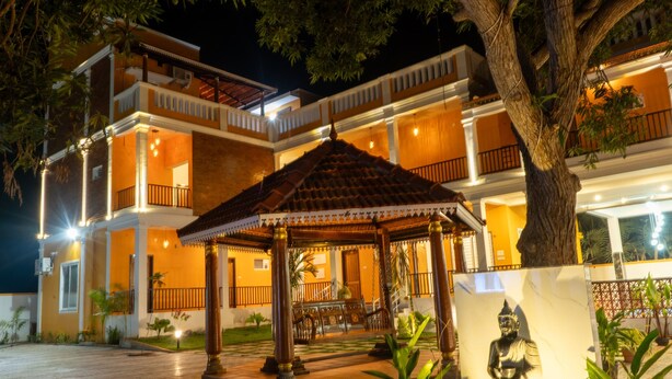 A multi-story building with a covered outdoor seating area, a statue, and a well-lit entrance. - DE ASIAN RESORT (Vanur)