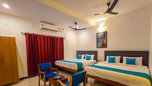 A hotel room with two beds, a desk with chairs, an air conditioning unit, a ceiling fan, and a painting on the wall. - DE ASIAN RESORT (Vanur)
