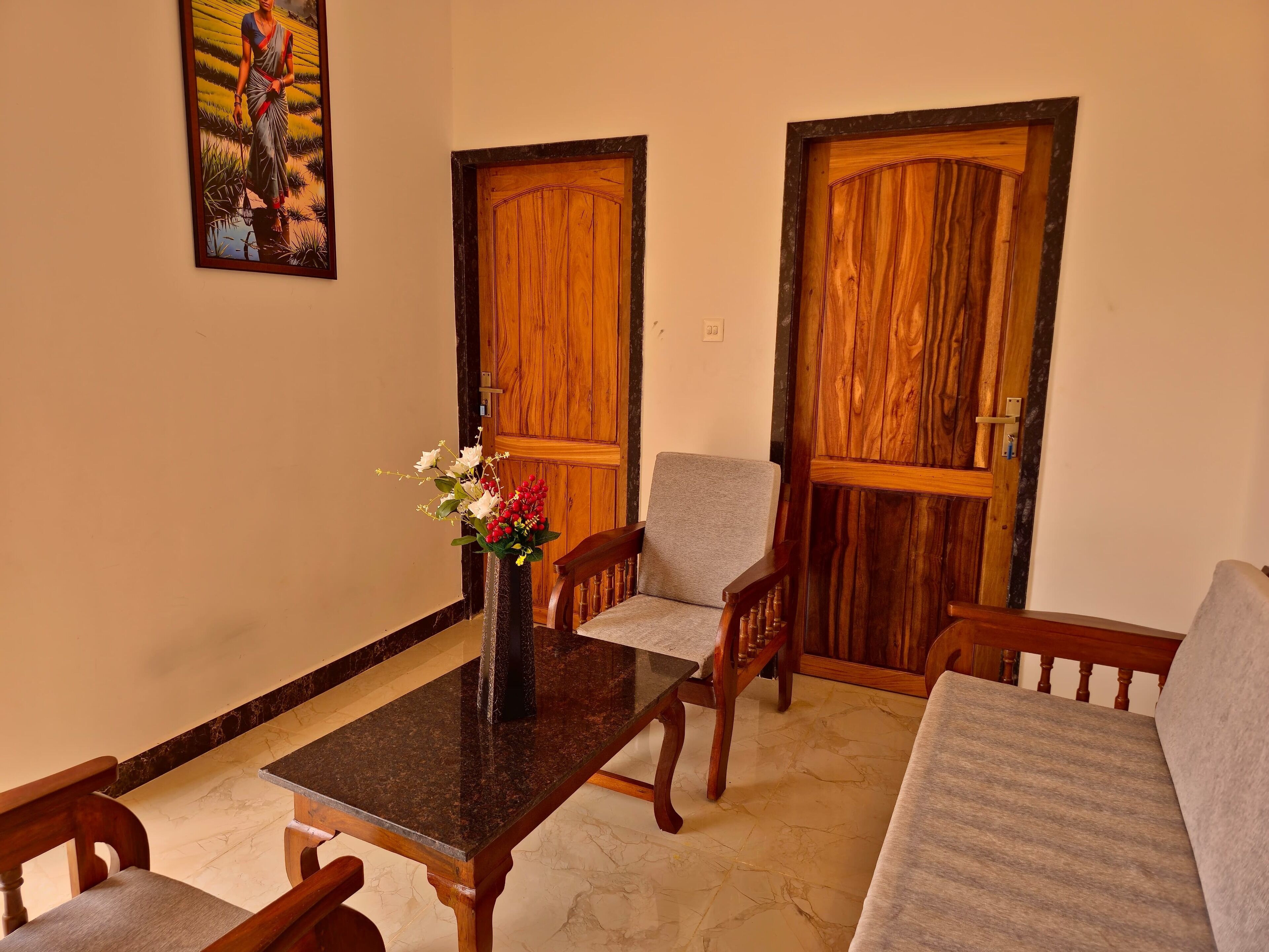 A room with a marble-tiled floor, a wooden table with a vase of flowers, two wooden doors, and a grey sofa.