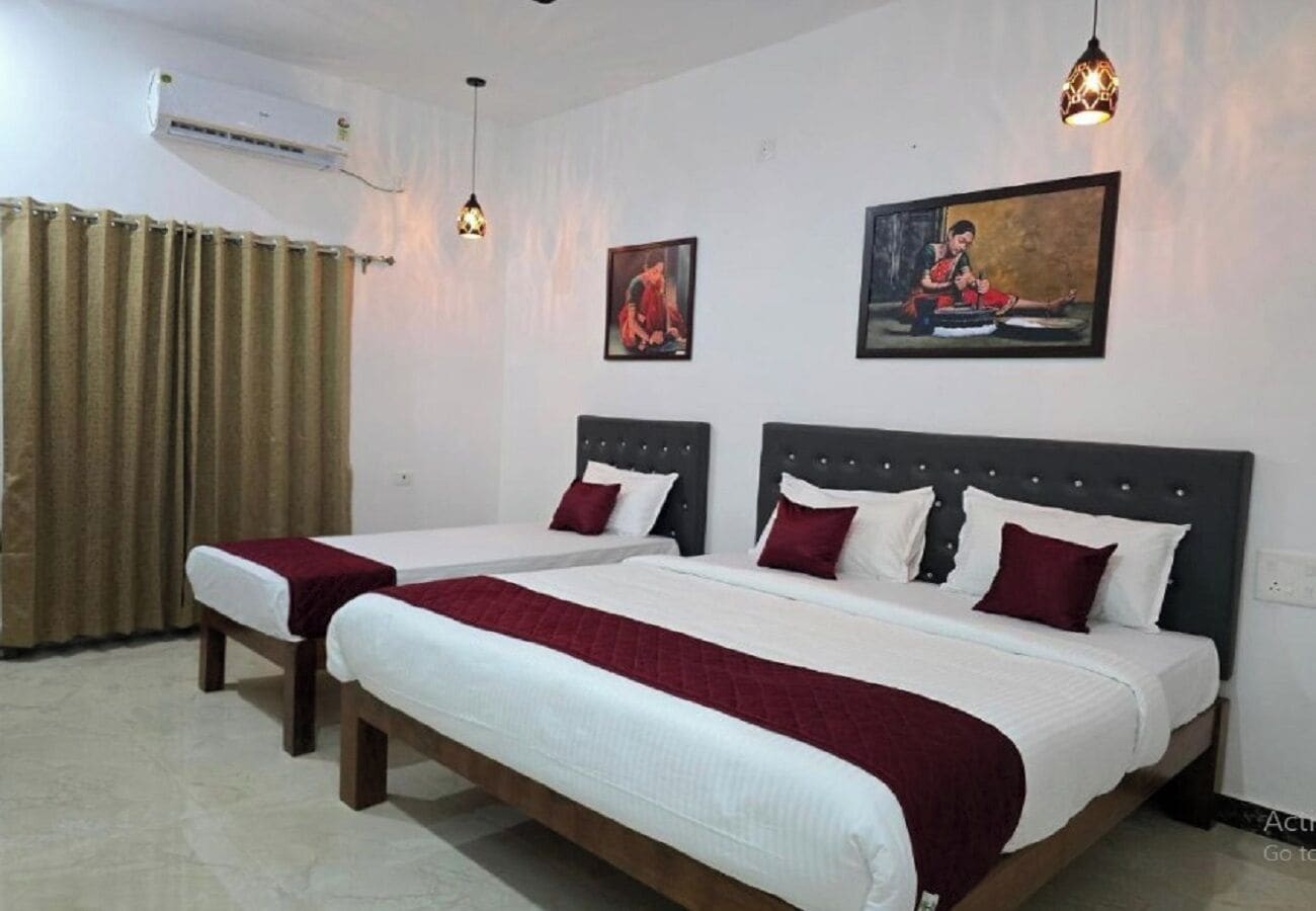 A hotel room with two beds, a large window with curtains, a wall-mounted air conditioner, and two wall-mounted pendant lights.