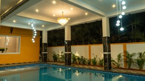 An indoor swimming pool with a tiled floor, surrounded by walls with a marble-like finish and a large window with a view of palm trees. - DE ASIAN RESORT (Vanur)