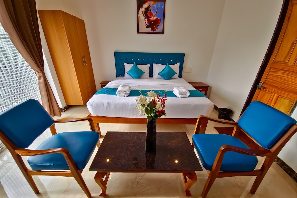 A hotel room with a bed, two blue chairs, a small table, and a vase with flowers.
