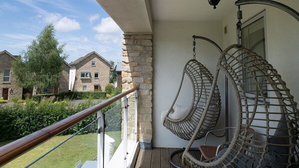A balcony with a wooden railing, a wicker chair, and a view of neighboring stone houses.