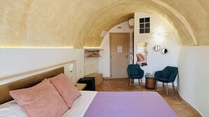 A bedroom with a large bed, a desk, two chairs, and an arched ceiling. - The Smile of the Sassi Rooms. Idris Superior Deluxe on Sassi view. (Matera)