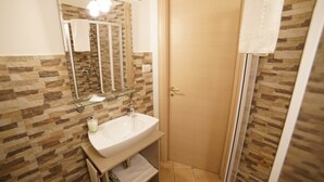 A bathroom with a glass shower enclosure, a sink with a mirror above it, and a door with a towel hanging on it. - The Smile of the Sassi Rooms. Idris Superior Deluxe on Sassi view. (Matera)
