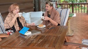 Ein Holztisch mit zwei Personen, die auf gestreiften Kissen sitzen, einem Laptop und einem Teller mit Essen.