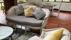 Ein Wohnzimmer mit einer Couch und zwei Sesseln, einem runden Tisch sowie einem Essbereich mit Stühlen.