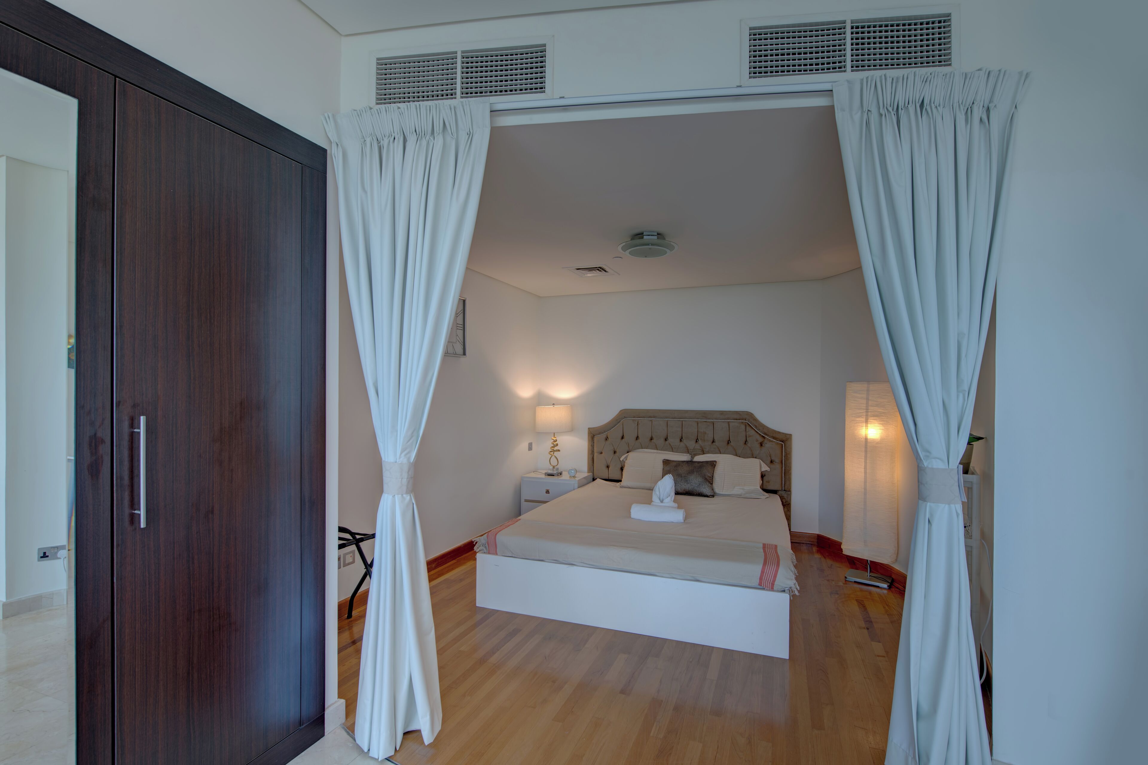 Een slaapkamer met een bed, nachtlampjes, een nachtkastje, een kledingkast en een raam met gordijnen.