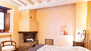 Une chambre avec une cheminée en briques, un lit recouvert d’une couvre-lit à motifs, une chaise et une table de chevet avec une lampe.