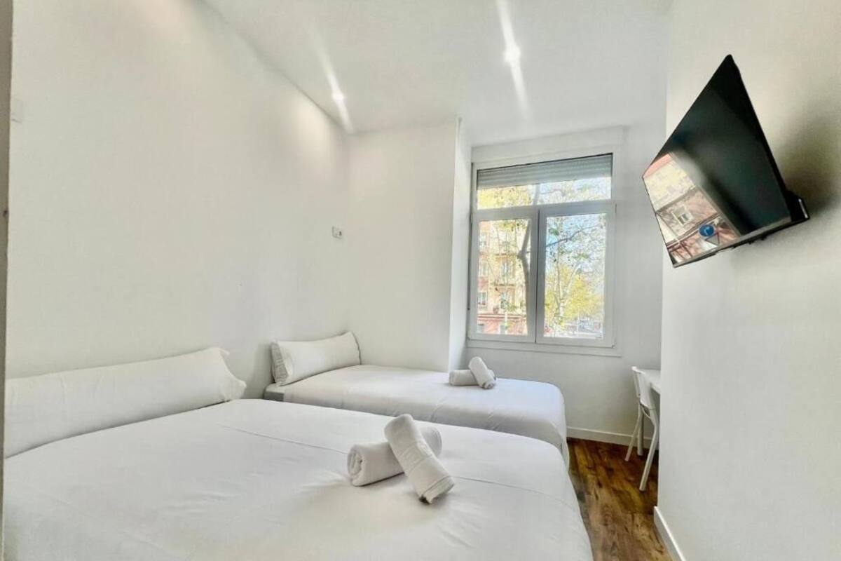 Ein Hotelzimmer mit zwei Betten, einem Fenster, einem flachbildfernseher an der Wand und Holzboden.