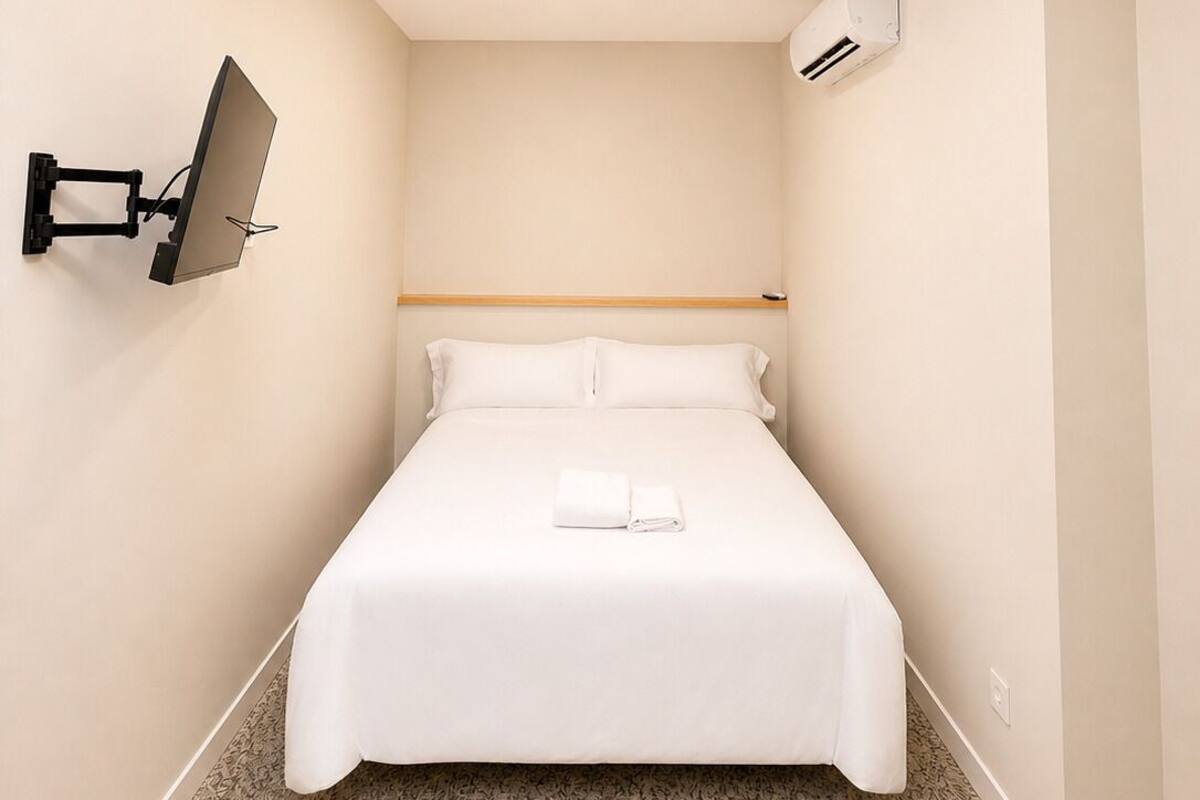 Ein Hotelzimmer mit Bett, einem an der Wand befestigten Fernseher, einer Klimaanlage und einem Oberlicht.