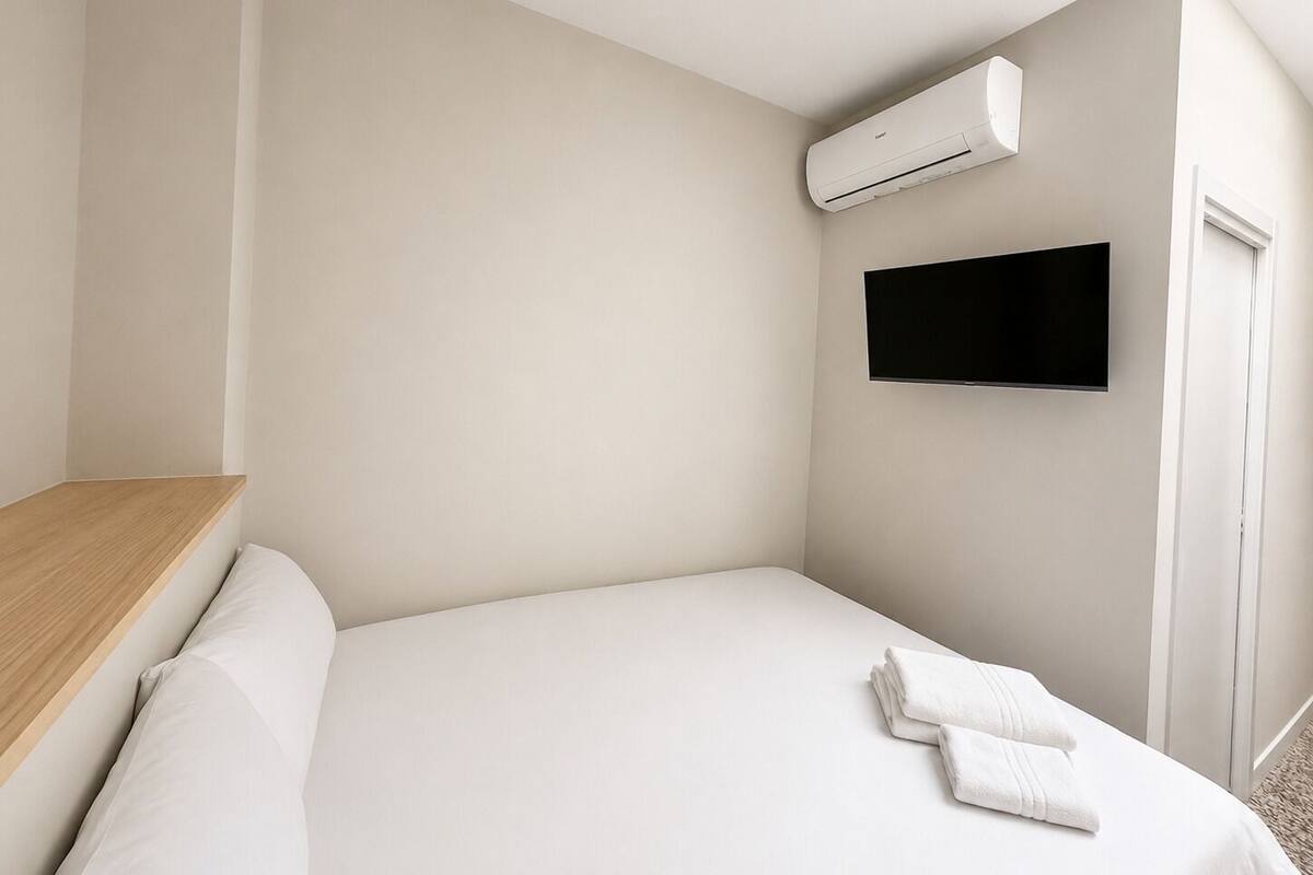Ein schlicht eingerichtetes Hotelzimmer mit Bett, einem Wand-Fernseher und einer Klimaanlage.