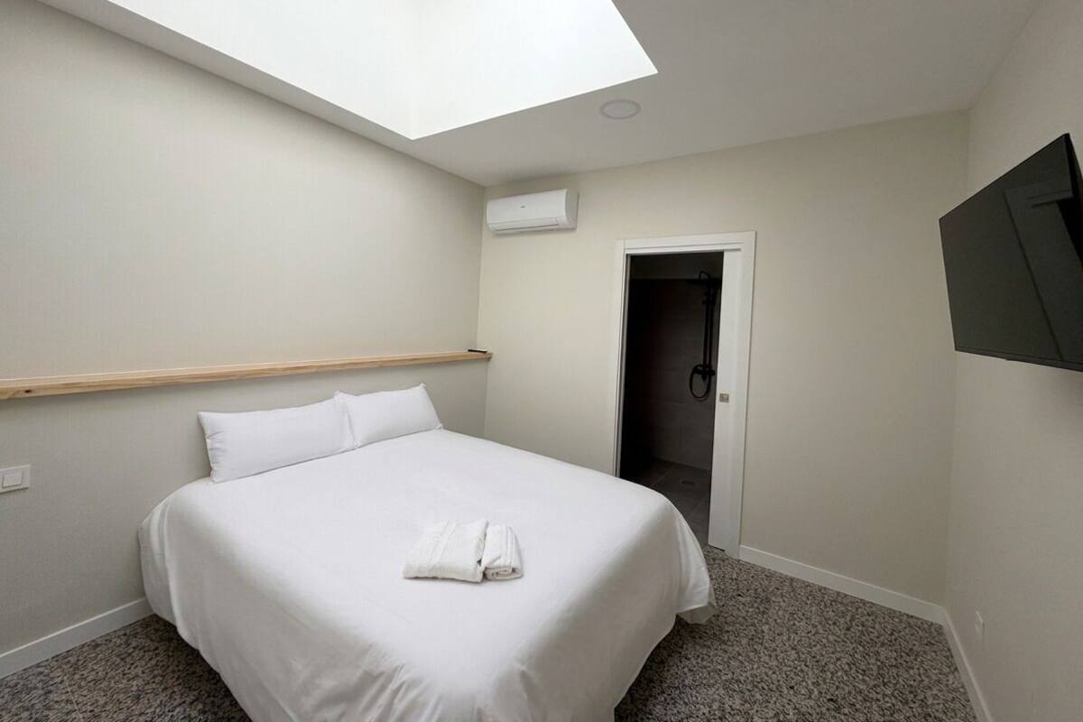 Ein Hotelzimmer mit Dachfenster, einem Bett, einer Dusche und einem an der Wand befestigten Fernseher.