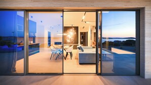 Et moderne interiør med spiseområde, sofa og udsigt gennem store glasdøre.