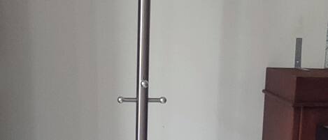 Un grand présentoir métallique à la base blanche, qui ressemble probablement à un porte-manteau, se trouve dans une pièce dont le mur est uni et qui contient une armoire en bois.