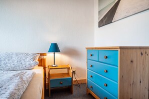 A bedroom with a bed, a nightstand with a lamp, and a blue dresser. - Apartment '3 Dg' with Shared Garden and Wi-Fi (Cuxhaven)