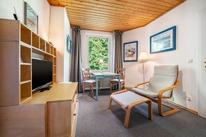 A cozy room with a television, a wooden cabinet, a table with chairs, a cushioned chair, and framed artwork on the walls. - Apartment '3 Dg' with Shared Garden and Wi-Fi (Cuxhaven)