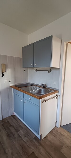 Une cuisine de taille réduite, dotée d’un plan de travail en bois, d’un évier et de meubles de couleur bleu clair.