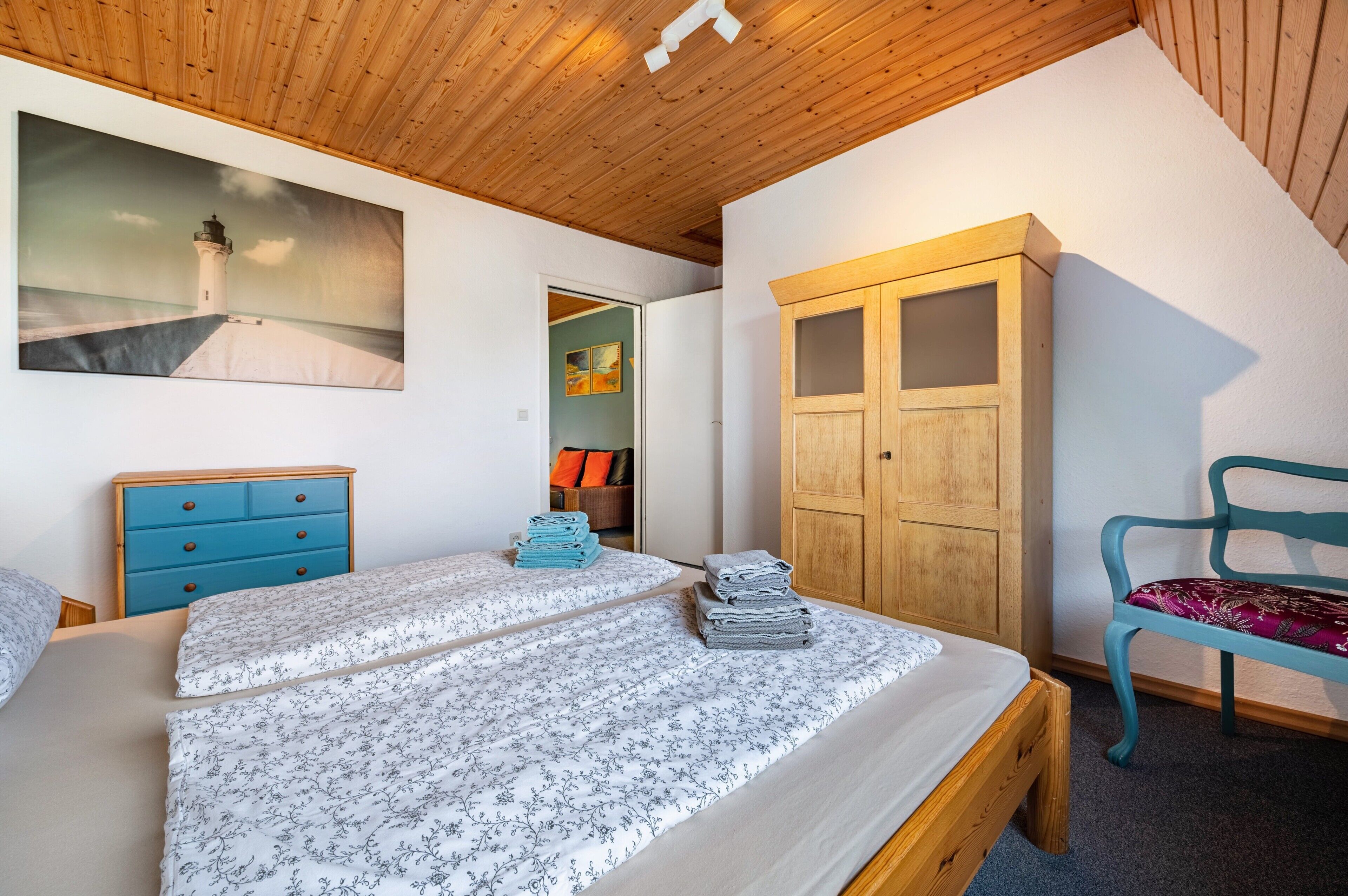 Ein Schlafzimmer mit einem Bett, einer blauen Kommode, einem Holzschrank und einem Sessel.