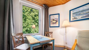 A room with a table and chairs, a window with curtains, a radiator, a lamp, and two framed artworks on the wall. - Apartment '3 Dg' with Shared Garden and Wi-Fi (Cuxhaven)