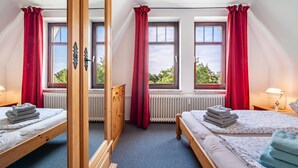 Ein Schlafzimmer mit zwei Betten, einem Holzschrank, einem Heizkörper und einem Fenster mit Vorhängen.