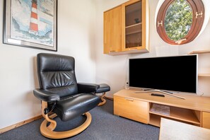 A room with a black leather recliner, a flat-screen TV on a wooden stand, a wooden cabinet, and a round window.