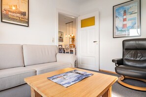 A living room with a sofa, a wooden table, a black leather chair, and a framed picture of a lighthouse. - Apartment '4 Dg' with Shared Garden and Wi-Fi (Cuxhaven)