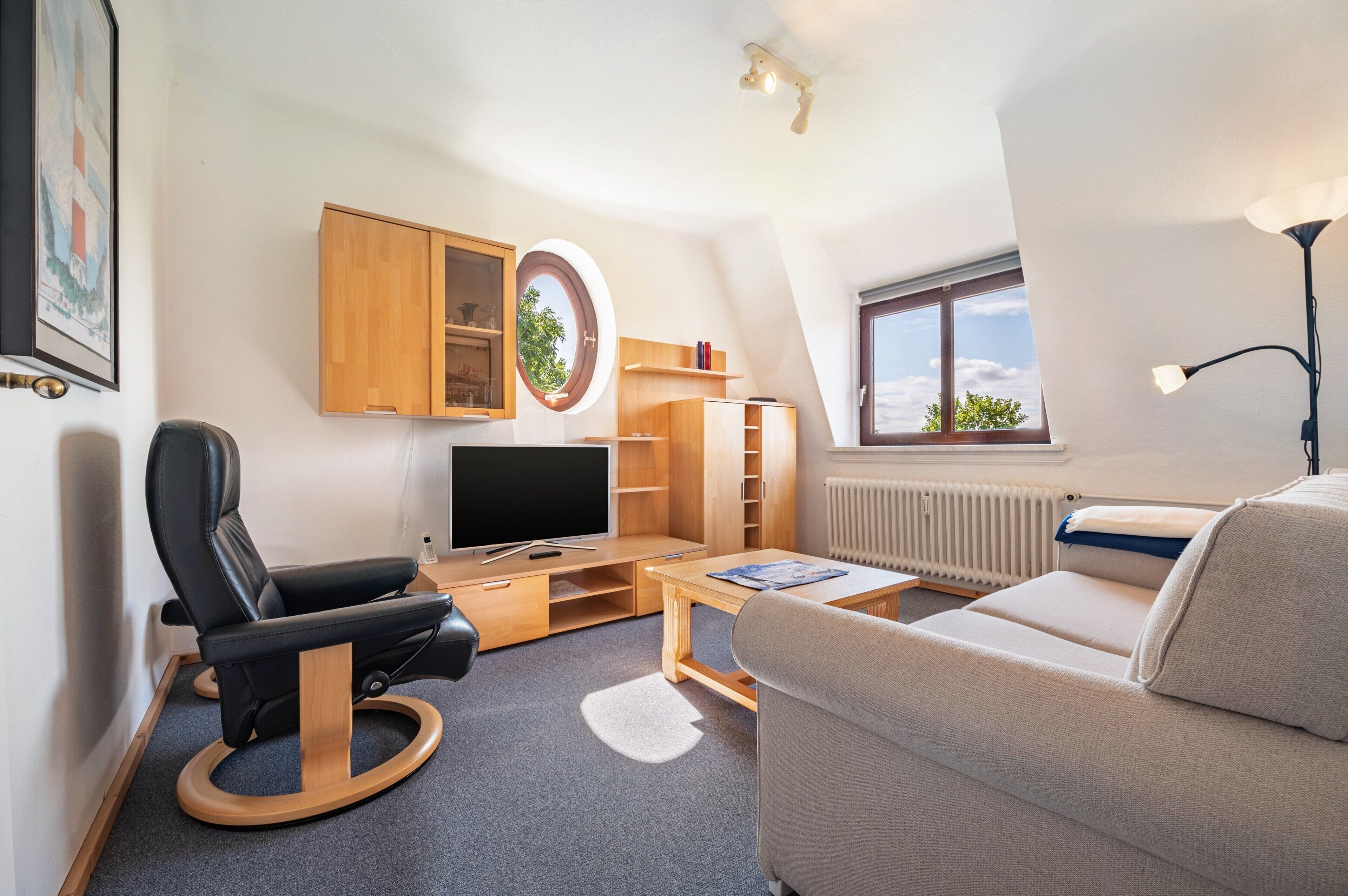 A modern, well-lit room with a television, wooden furniture, a sofa, and a window with a view.