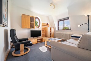 A modern, well-lit room with a television, wooden furniture, a sofa, and a window with a view. - Apartment '4 Dg' with Shared Garden and Wi-Fi (Cuxhaven)