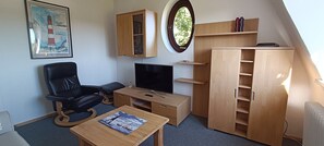 Una habitación funcional con escritorio, silla, televisor, armarios de madera y ventana.