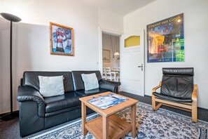 A living room with a black leather sofa, a wooden coffee table, and a black leather armchair. There are two framed artworks on the walls.