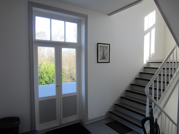 Eine Treppe mit weißen Geländern führt zu einer Zwischenebene, eine Tür mit Glasfeldern und ein gerahmtes Bild an der Wand.