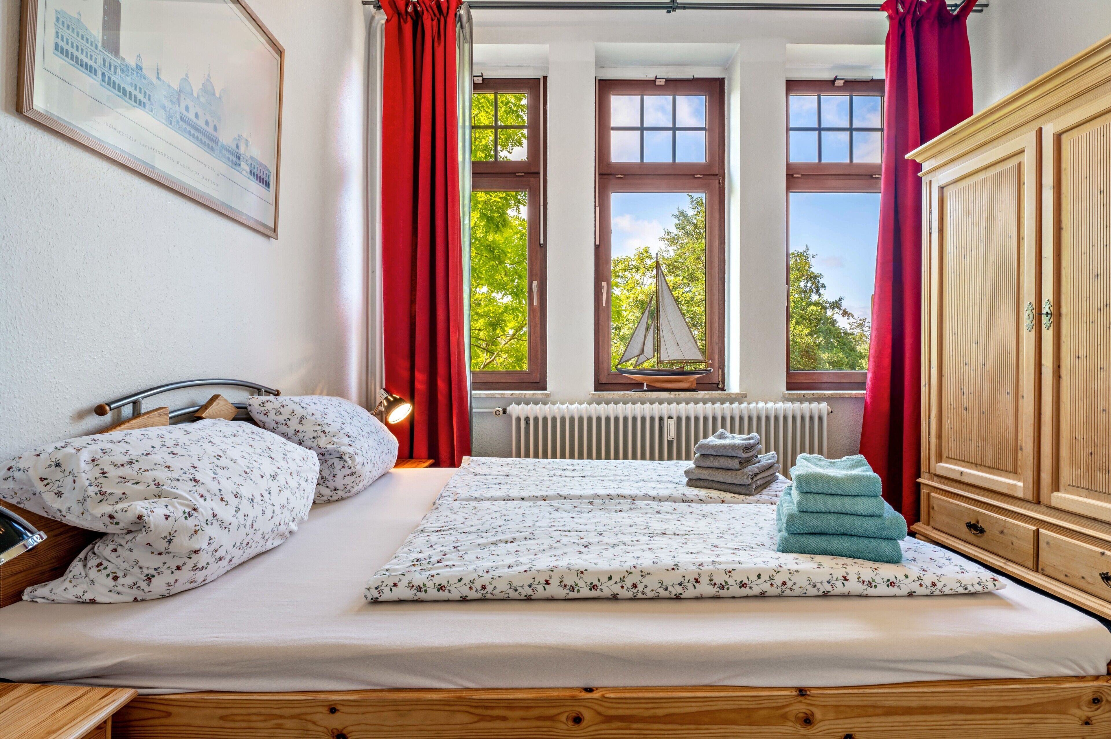A bedroom with a bed, a radiator, a window with curtains, and a view of trees.