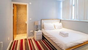 A bedroom with a bed, nightstand, lamp, and a window with blinds. - 2 Bedroom City Apartment (Sheffield)