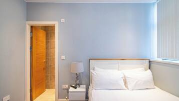 Quarto de hotel com uma cama, mesa de cabeceira, abajur e porta para um banheiro.