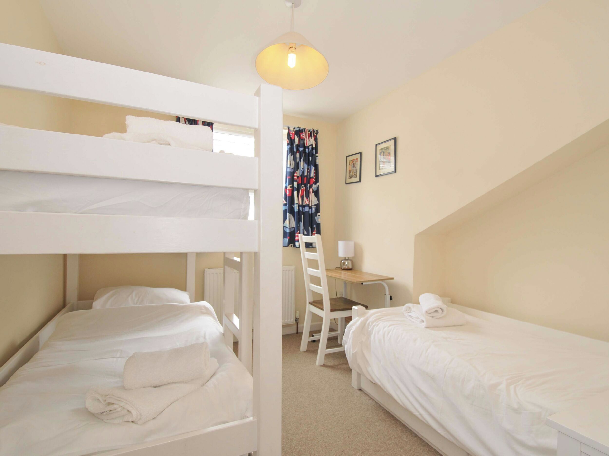 A dormitory room with bunk beds, a desk, a chair, and a lamp.