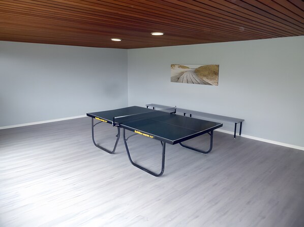 Una mesa de ping pong en una habitación con paredes grises claras y techo de madera.