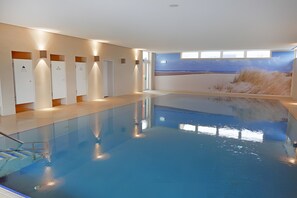 Una piscina interior con vistas claras a la playa a través de la ventana.