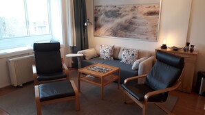 Una sala de estar moderna con un sofá, dos sillones, una mesita de centro, un radiador y un ventanal grande.