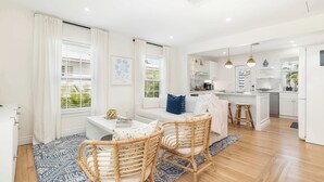 A modern living room with a sofa, two wicker chairs, a coffee table, and a kitchen area with white cabinets and a dining island.