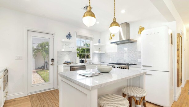 A modern kitchen with white cabinetry, a central island with stools, a built-in oven, and a white refrigerator.