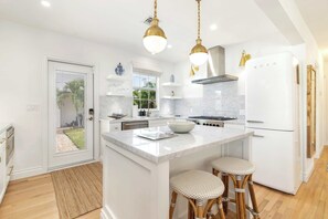 A modern kitchen with white cabinetry, a central island with stools, a built-in oven, and a white refrigerator. - The Blue Door I By Hotel Home Stays (West Palm Beach)
