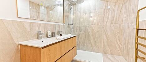 A modern bathroom with a marble shower, a wooden vanity, and a large mirror.
