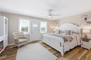 Ein Schlafzimmer mit Bett, Stuhl, Deckenventilator und einer Tür mit Fenstern.