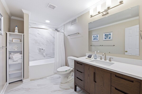 Un baño con bañera, inodoro, tocador con lavamanos y cortina de ducha.