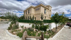 A hostel building with a balcony, surrounded by greenery and a paved area. - Full Of Life (Nevşehir)