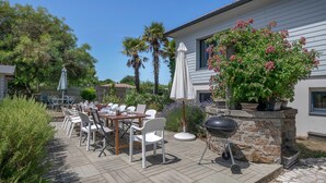 Un patio al aire libre con una mesa, sillas, una parrilla y plantas en macetas.
