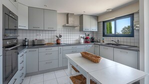 Una cocina moderna con armarios grises, horno integrado, encimera blanca y una ventana que proporciona luz natural.