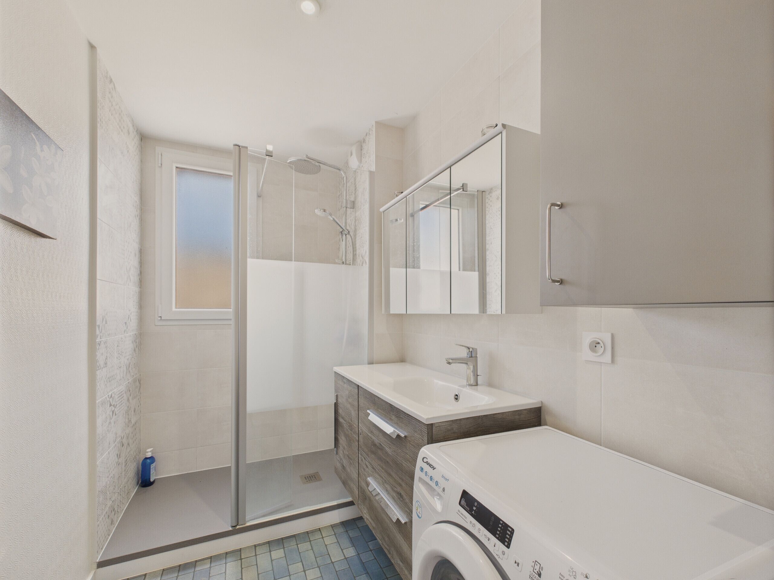 A modern bathroom with a glass-enclosed shower, a built-in sink, and a washing machine.